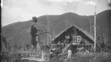 E. St. Vráz se síťkou na chytání hmyzu před velkou obytnou chýší označenou vlajkou s českým lvem a nápisem Vraz v pohoří Hattam. Nová Guinea, 1896