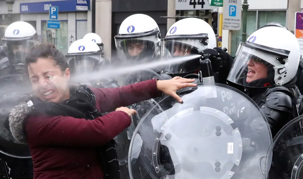 Policista při zásahu slzným plynem proti ženě během protestů tzv. „žlutých vest“ v Bruselu.