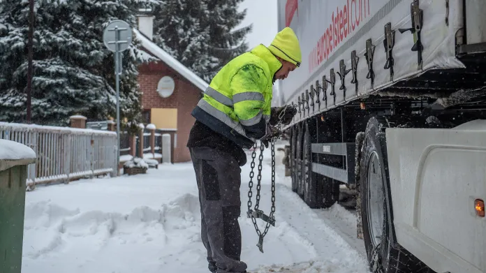 Řidič kamionu nasazuje sněhové řetězy