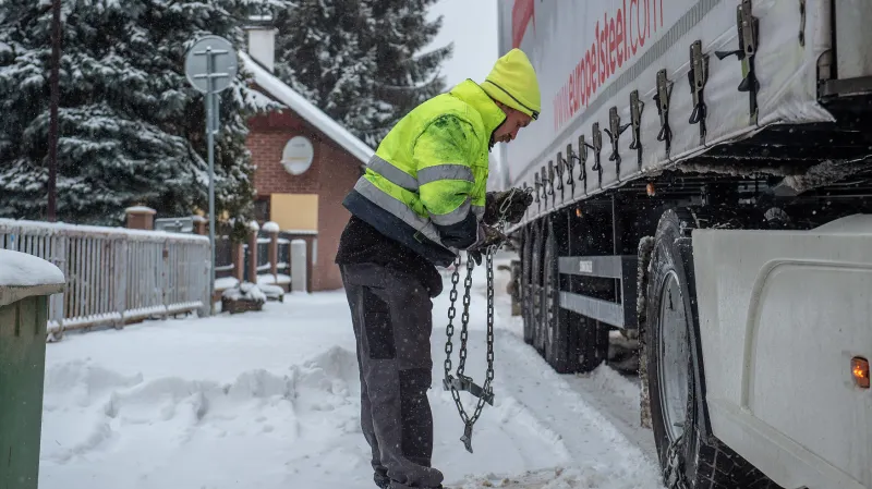Řidič kamionu nasazuje sněhové řetězy