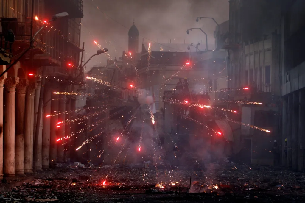 Iráčtí demonstranti házejí pyrotechniku směrem k iráckým bezpečnostním silám během protivládních protestů v Bagdádu