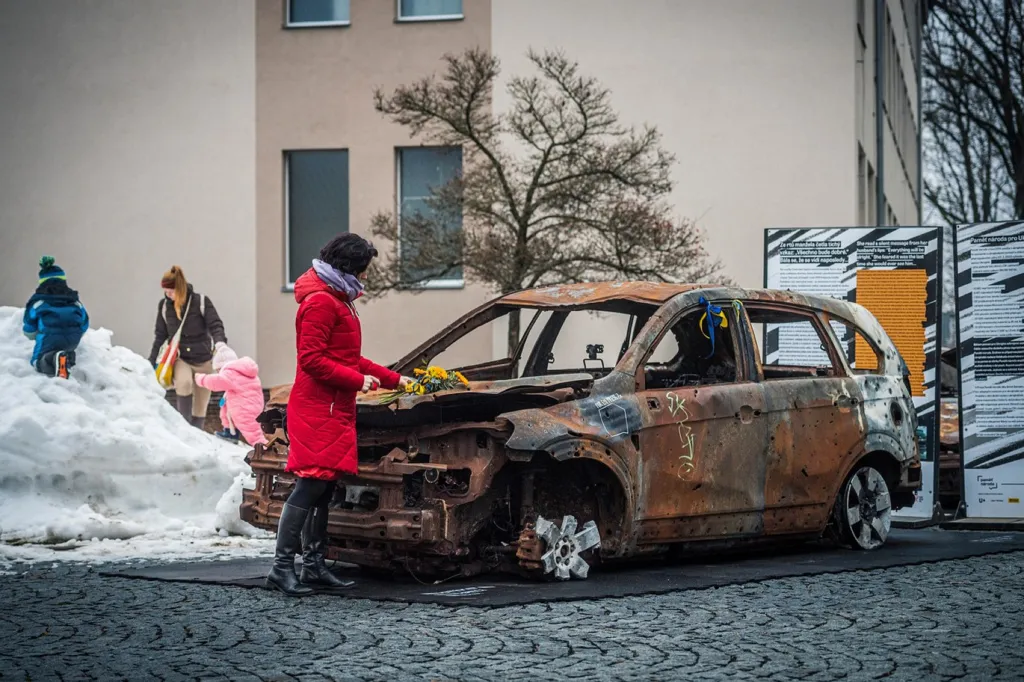 Návštěvnice výstavy zapaluje na kapotě auta svíčku