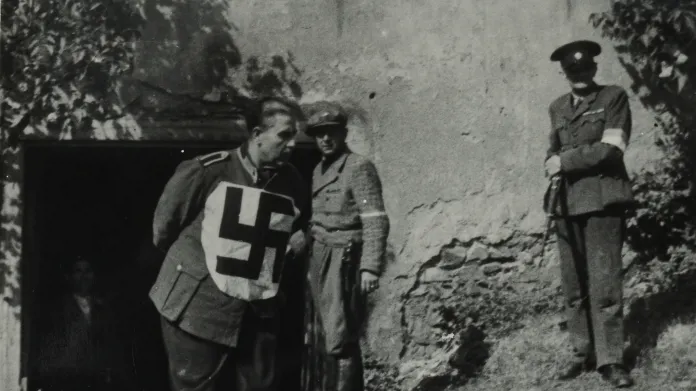 Německý zajatec s hákovým křížem na prsou vychází ze sklepa v Tichém údolí. U vchodu stojí muž v civilu, nad ním muž v uniformě a s puškou v ruce