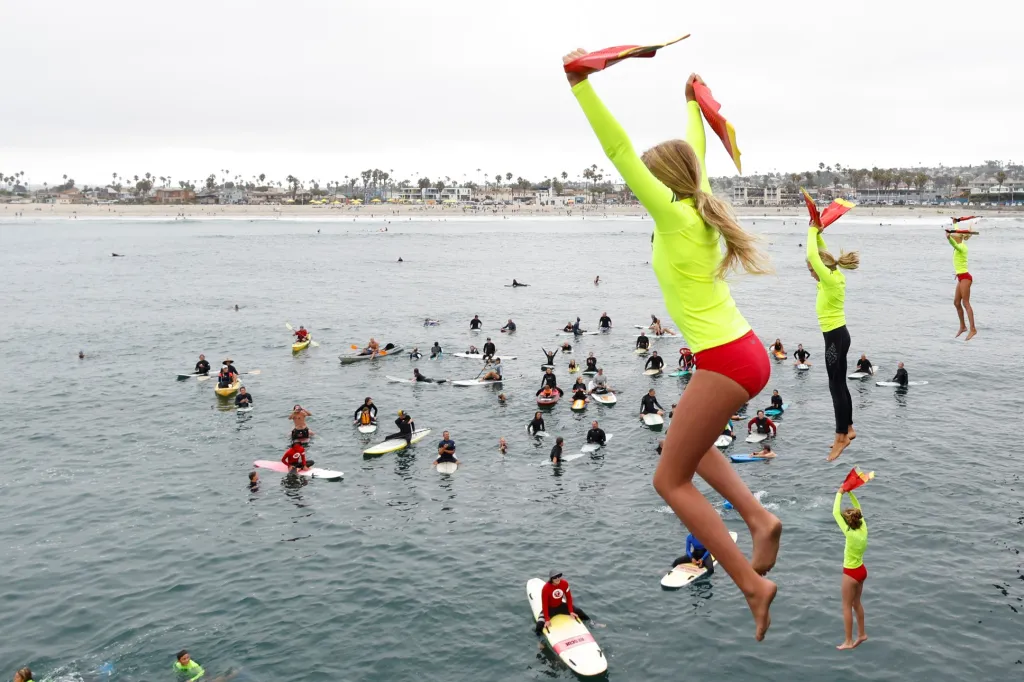 Účastníci programu „San Diego Junior Lifeguard“ skáčou ze strážních věží do vody během každoročního křtu nových vodních záchranářů v Ocean Beach v Kalifornii