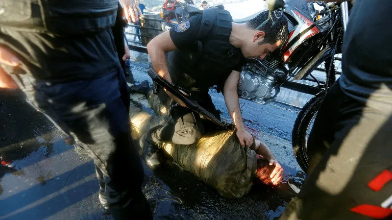 Policista kontroluje jednoho z vojáků, kterého zlynčoval dav Erdoganových stoupenců