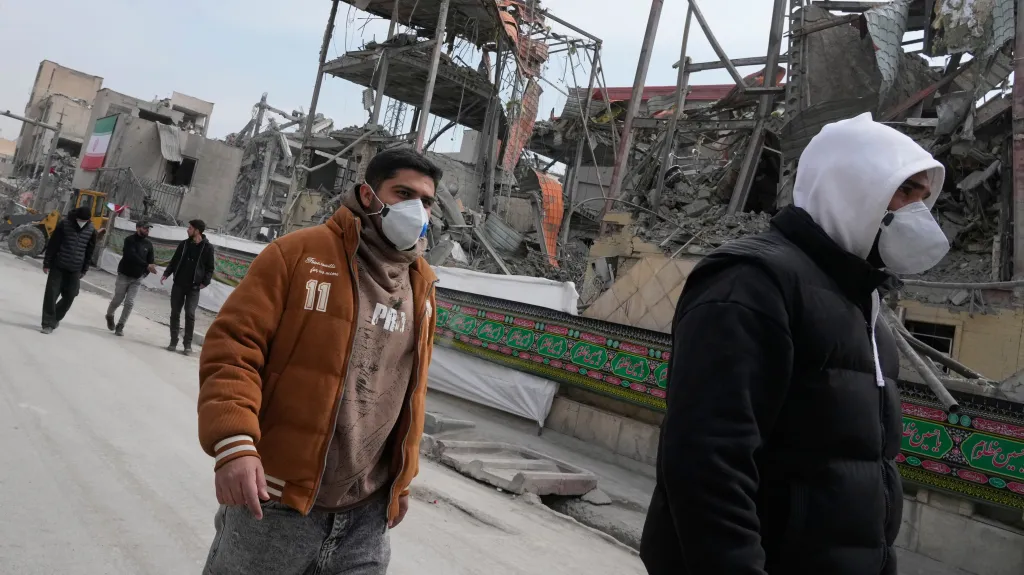 Muži v Teheránu procházejí kolem budovy zničené americko-izraelským bombardováním